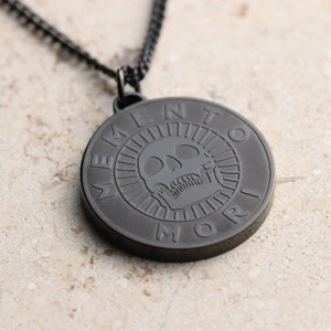 May include: Black pendant necklace with a skull and the words "Memento Mori" engraved on a round disc.