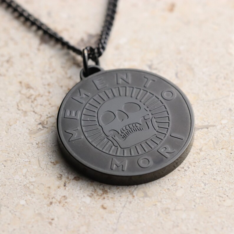 May include: Black pendant necklace with a skull and the words "Memento Mori" engraved on a round disc.