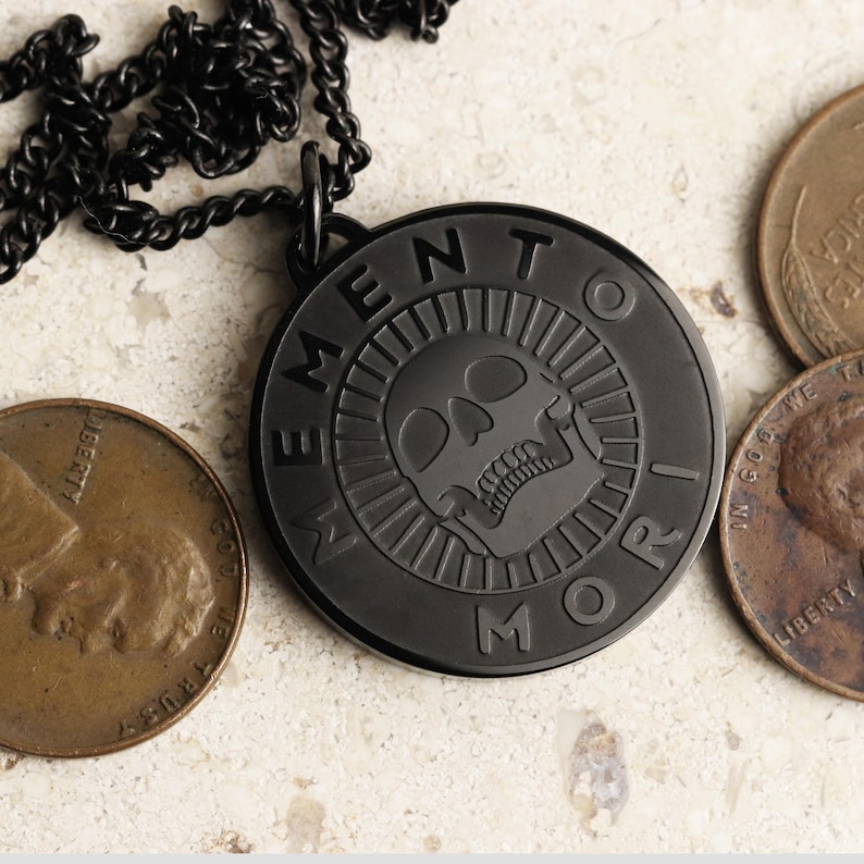 May include: Black necklace with a round pendant featuring a skull and the words "Memento Mori" in a circular design.