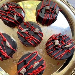 May include: Five chocolate-covered cookies decorated with red and black sprinkles, tombstones, and the words "RIP".