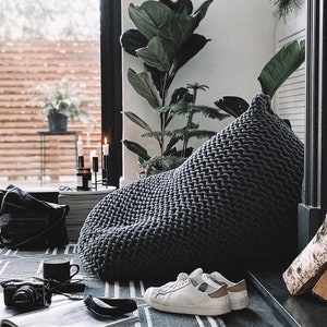 large grey knitted beanbag chair sitting in the corner of a contemporary living room space with plants in the background