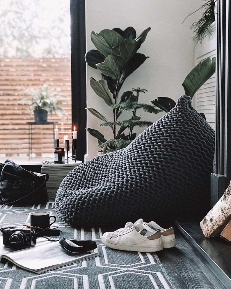 large grey knitted beanbag chair sitting in the corner of a contemporary living room space with plants in the background