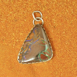 Peut inclure: Un pendentif en argent avec une opale triangulaire de couleur brun foncé et des reflets irisés bleus, verts et violets. L'opale est sertie dans une bélière en argent avec un bord festonné.