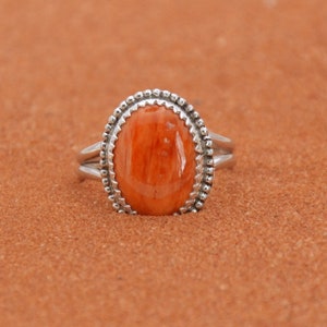 Op de afbeelding: Een zilveren ring met een ovale, oranje steen die is gezet in een geperde bezel.