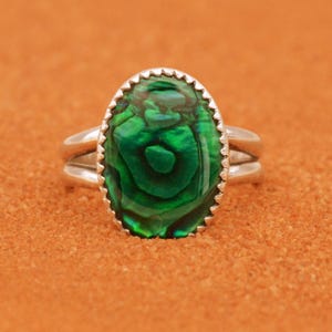 Peut inclure: Une bague en argent avec une incrustation de nacre d'ormeau verte. La bague a une bande simple avec un détail de double bande.
