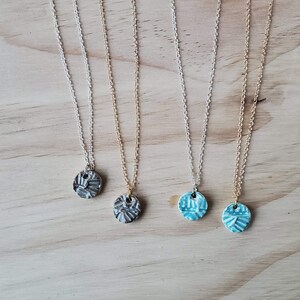 May include: Three necklaces with different colored ceramic pendants. The pendants are round and have a textured design. The necklaces are on a wooden surface.