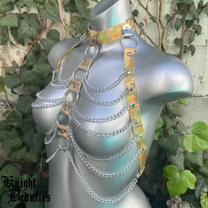May include: A gold and iridescent chainmail harness with silver chains. The harness has a choker style neckline and multiple straps that connect to the chains.