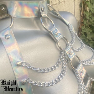May include: A silver harness with iridescent accents, featuring a choker, shoulder straps, and dangling chains. The harness has metal rings and is secured with rivets. The text "Knight Beauties" is visible at the bottom left.