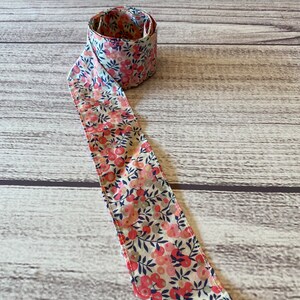 Puede incluir: Una cinta de tela blanca con un estampado floral rosa y azul. La cinta est&aacute; enrollada y anudada.