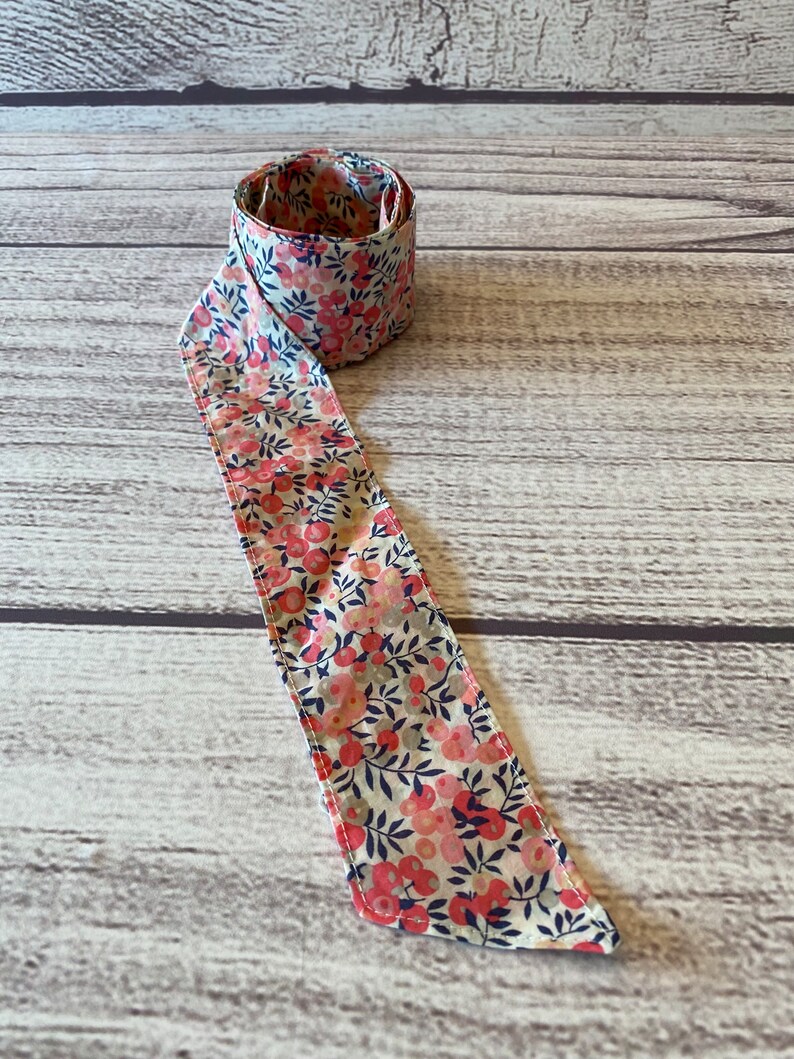 Puede incluir: Una cinta de tela blanca con un estampado floral rosa y azul. La cinta est&aacute; enrollada y anudada.