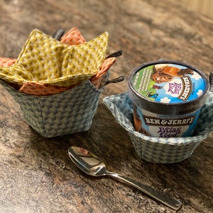 Op de afbeelding: Twee stoffen kom-cozies, een blauwe met witte stippen en een met een geel en oranje bloemenpatroon, met een pint Ben & Jerry's ijs in de blauwe cozy.