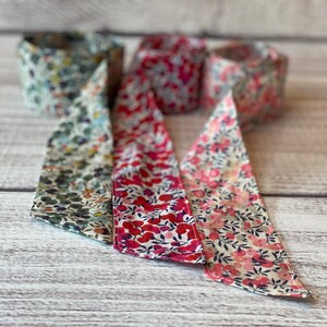 Puede incluir: Tres rollos de cinta de tela con patrones florales. Los rollos son en tonos de verde, rosa y rojo.