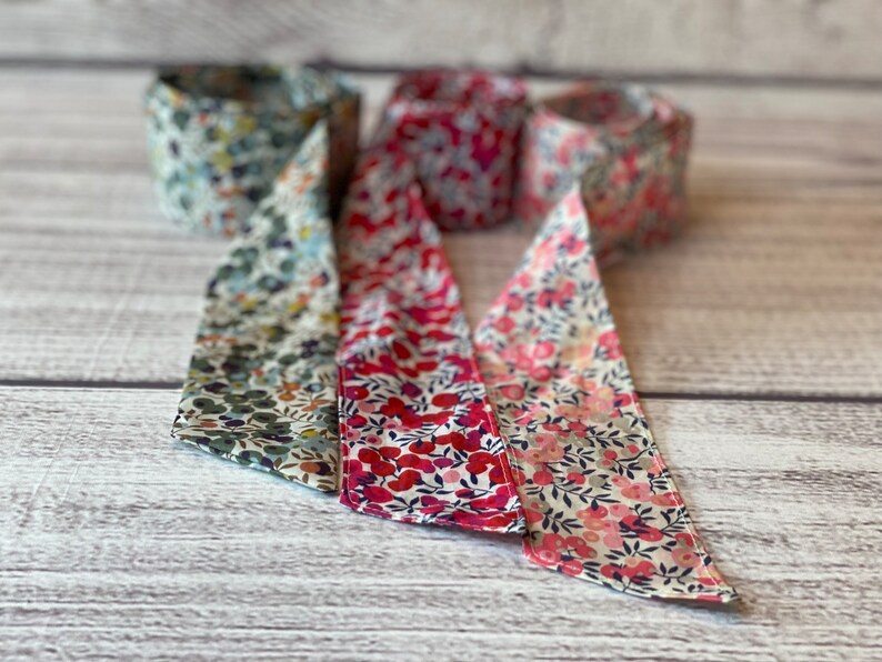 Puede incluir: Tres rollos de cinta de tela con patrones florales. Los rollos son en tonos de verde, rosa y rojo.