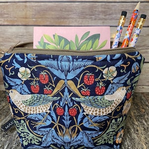 May include: A fabric zipper pouch featuring a dark blue background with a repeating pattern of birds, strawberries, and foliage in shades of light blue, green, and red. Three patterned pencils and a pink card with green leaves are inside.