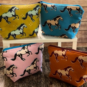 Może przedstawiać: Cztery różne materiałowe kosmetyczki z zamkiem błyskawicznym z nadrukiem konia. Kosmetyczki są w kolorze żółtym, niebieskim, różowym i brązowym. Kosmetyczki są wszystkie tego samego rozmiaru i kształtu.