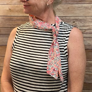 Puede incluir: Una mujer con una camisa sin mangas a rayas con una bufanda de estampado floral rosa y blanco atada alrededor del cuello.
