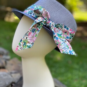 May include: A blue linen hat with a floral print ribbon tied in a bow. The hat is on a white mannequin head.