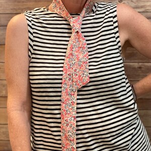 Puede incluir: Una camisa sin mangas a rayas con una corbata de estampado floral. La corbata est&aacute; anudada en el cuello.