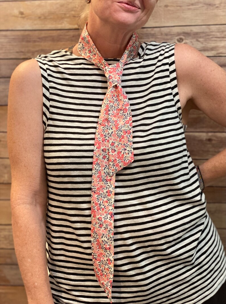 Puede incluir: Una camisa sin mangas a rayas con una corbata de estampado floral. La corbata est&aacute; anudada en el cuello.