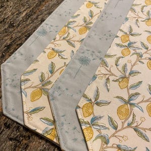 May include: Set of four hexagon-shaped placemats with a lemon and dandelion print. The placemats are made of a light blue fabric with a white and yellow floral pattern.
