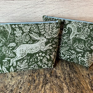 May include: Two green zippered pouches with white woodland animal prints. One pouch features a rabbit and the other features a squirrel.