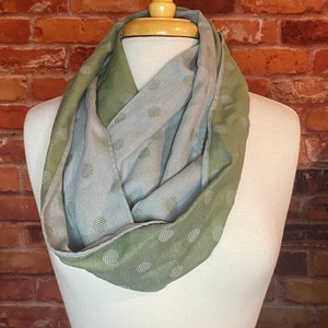 May include: A green and gray infinity scarf with a polka dot pattern. The scarf is made of a soft, lightweight fabric and is perfect for adding a touch of style to any outfit.