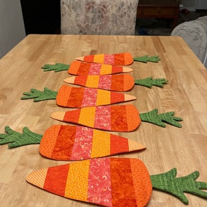 May include: Six orange and green carrot-shaped placemats with a striped pattern. The placemats are made of fabric and have a quilted texture.