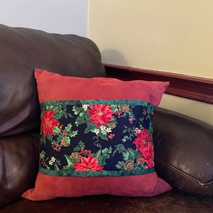 May include: A red and green Christmas-themed throw pillow with a floral pattern on a dark brown leather couch.
