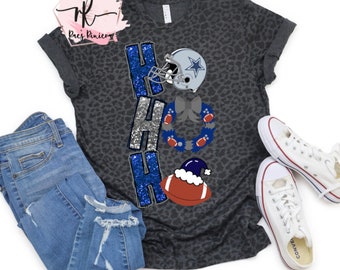 Puede incluir: Una camiseta gris con estampado de leopardo. La camiseta presenta un diseño brillante azul y plateado "HO HO HO" con un casco de fútbol, una corona y un balón de fútbol con un gorro de Papá Noel.