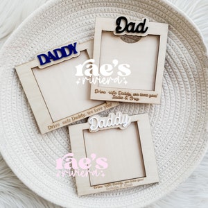 May include: Three wooden picture frames with the words "Daddy", "Dad", and "Daddy" in different fonts and colors. Each frame has a space for a photo and a personalized message below the photo. The message reads "Drive safe Daddy, we love you!" with the names of the senders below.