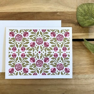May include: A white card with a repeating pattern of pink and burgundy roses with green leaves and stems on a white background.