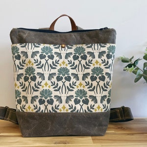 May include: A brown canvas backpack with a zippered top and a front pocket. The backpack has a floral pattern with green leaves, yellow flowers, and blue butterflies.