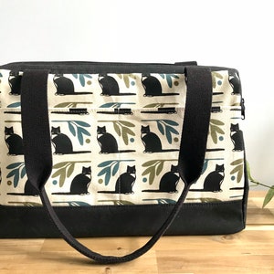 May include: A black canvas tote bag with black straps and a cream-coloured fabric lining featuring a repeating pattern of black cats, green leaves, and blue circles.