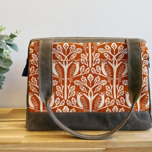 May include: A brown canvas tote bag with a zipper closure and two top handles. The bag features a white and orange print of owls in trees.