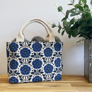 May include: A white canvas tote bag with blue floral print. The bag has two handles and is filled with yarn.