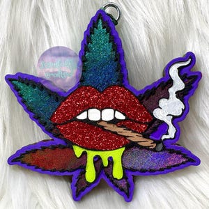 Könnte beinhalten: Ein glitzerndes Cannabisblatt-Design in Lila, Grün und Rot mit roten Lippen, die einen Joint rauchen. Die Lippen haben weiße Zähne und tropfen mit neon-grünem Schleim. Oben befindet sich ein silberner Ring.