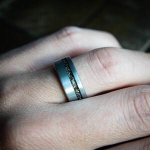 May include: A silver ring with a band of embedded dark gray stones.