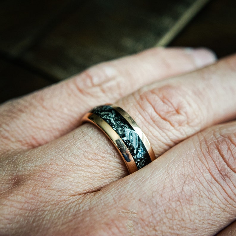 May include: A gold ring with a black and white inlay. The ring is worn on a person's finger.