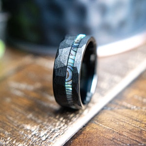 May include: A black tungsten carbide ring with a hammered finish and a thin inlay of iridescent abalone shell.