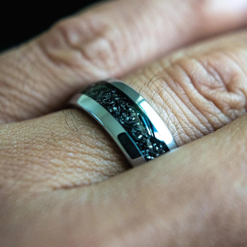 K&ouml;nnte beinhalten: Ein silberner Ring mit einer schwarzen Einlage. Die Einlage hat ein strukturiertes, gewebtes Muster.