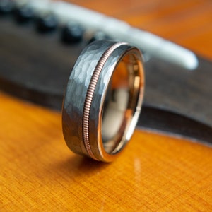 May include: A silver and rose gold wedding band with a hammered finish and a thin rose gold band around the edge.
