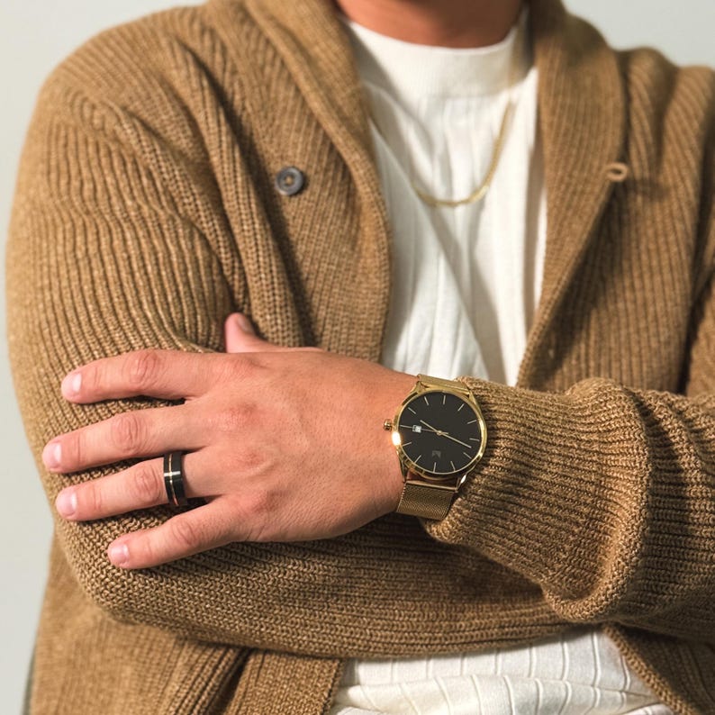 May include: A person wearing a brown cardigan with a gold watch and a black ring on their finger.