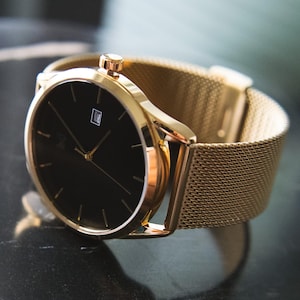 May include: A gold-tone watch with a black face and a mesh metal strap.