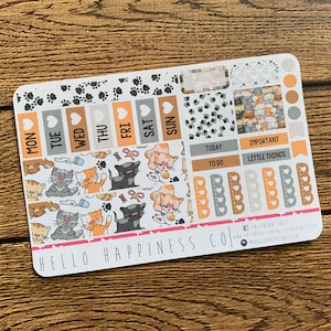 May include: A set of cat-themed planner stickers with paw prints, hearts, and days of the week. The stickers are on a white background with the text "HELLO HAPPINESS CO."