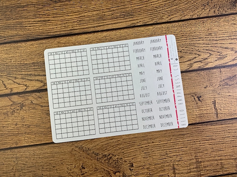 May include: A white sheet of paper with a grid of squares for each month of the year. The months are listed on the right side of the sheet with the text "HELLO HAPPINESS CO."