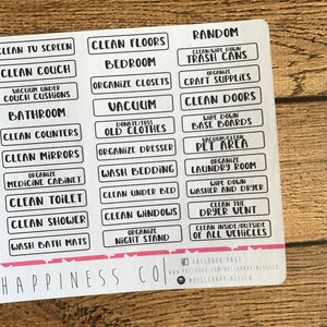 May include: A sheet of white rectangular labels with black text for home organisation. Labels include "Clean Floors", "Bedroom", "Organise Closets", "Vacuum", and "Clean Doors". The bottom of the sheet has the text "Happiness Co".