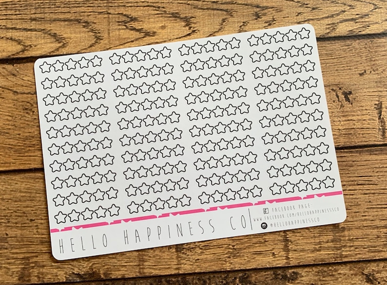 Puede incluir: Una hoja de papel adhesivo blanco con 100 pegatinas de estrellas de contorno negro. La hoja tiene el texto "HELLO HAPPINESS CO" impreso en la parte inferior. El texto "FACEBOOK PAGE" est&aacute; impreso en la esquina inferior derecha.