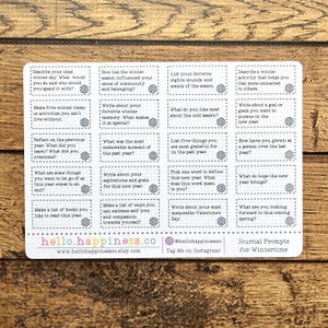 May include: A set of 16 printable journal prompts for wintertime. The prompts are printed on a white background with a gray grid pattern. The prompts are organized into four columns and four rows. Each prompt is enclosed in a gray box with a snowflake design in the corner. The prompts are designed to help you reflect on the past year, set goals for the new year, and appreciate the beauty of winter.