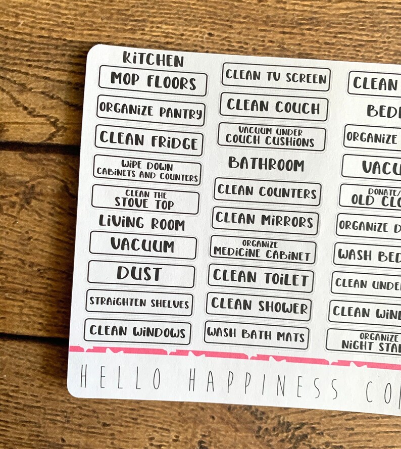 May include: A sheet of white cleaning labels with black text. Labels include "Kitchen", "Mop Floors", "Clean Fridge", "Vacuum", and "Clean Windows". The bottom of the sheet has the text "Hello Happiness Co" in a handwritten font.