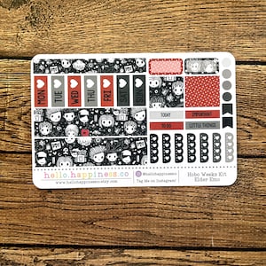 May include: A sticker sheet with a black and white design featuring cartoon characters and various shapes. Red accents highlight the days of the week, and other labels. The sheet includes the text "hello.happiness.co" and "Hobo Weeks Kit Elder Emo".